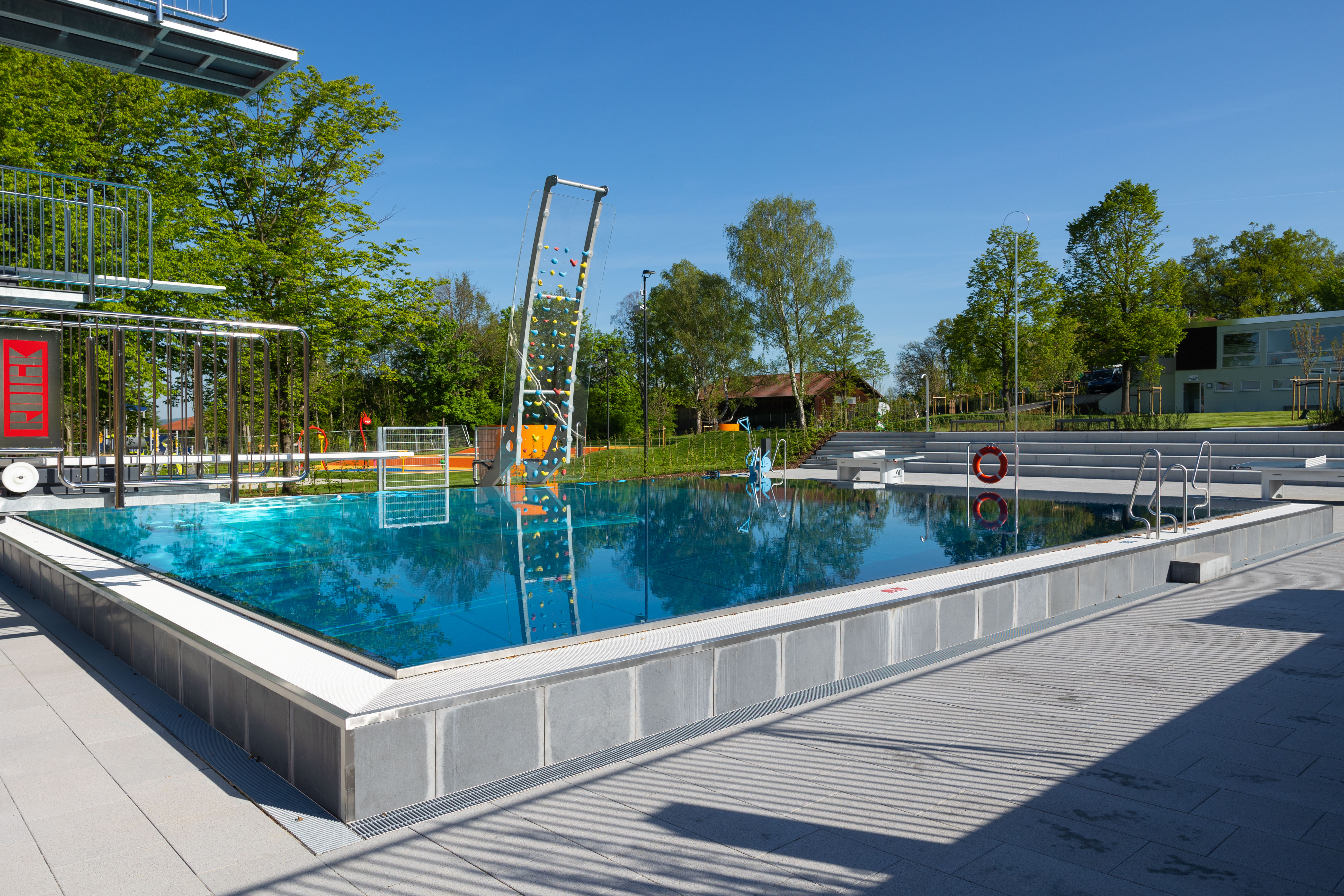 Ein Freibad mit Wasserfläche und Kletterwand im Hintergrund.