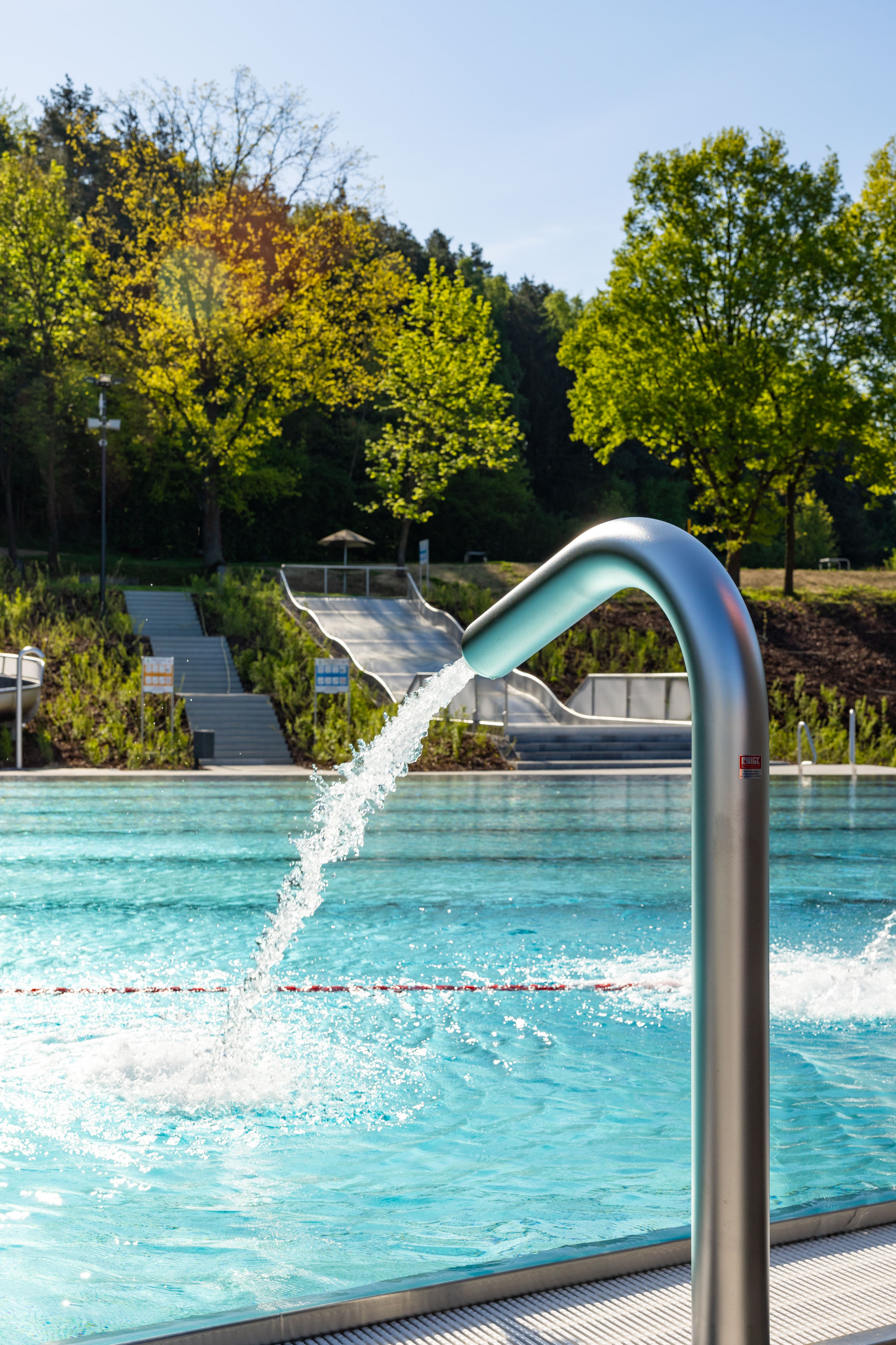 Sprudelnde Wasserfontäne im Freibad mit Bäumen im Hintergrund