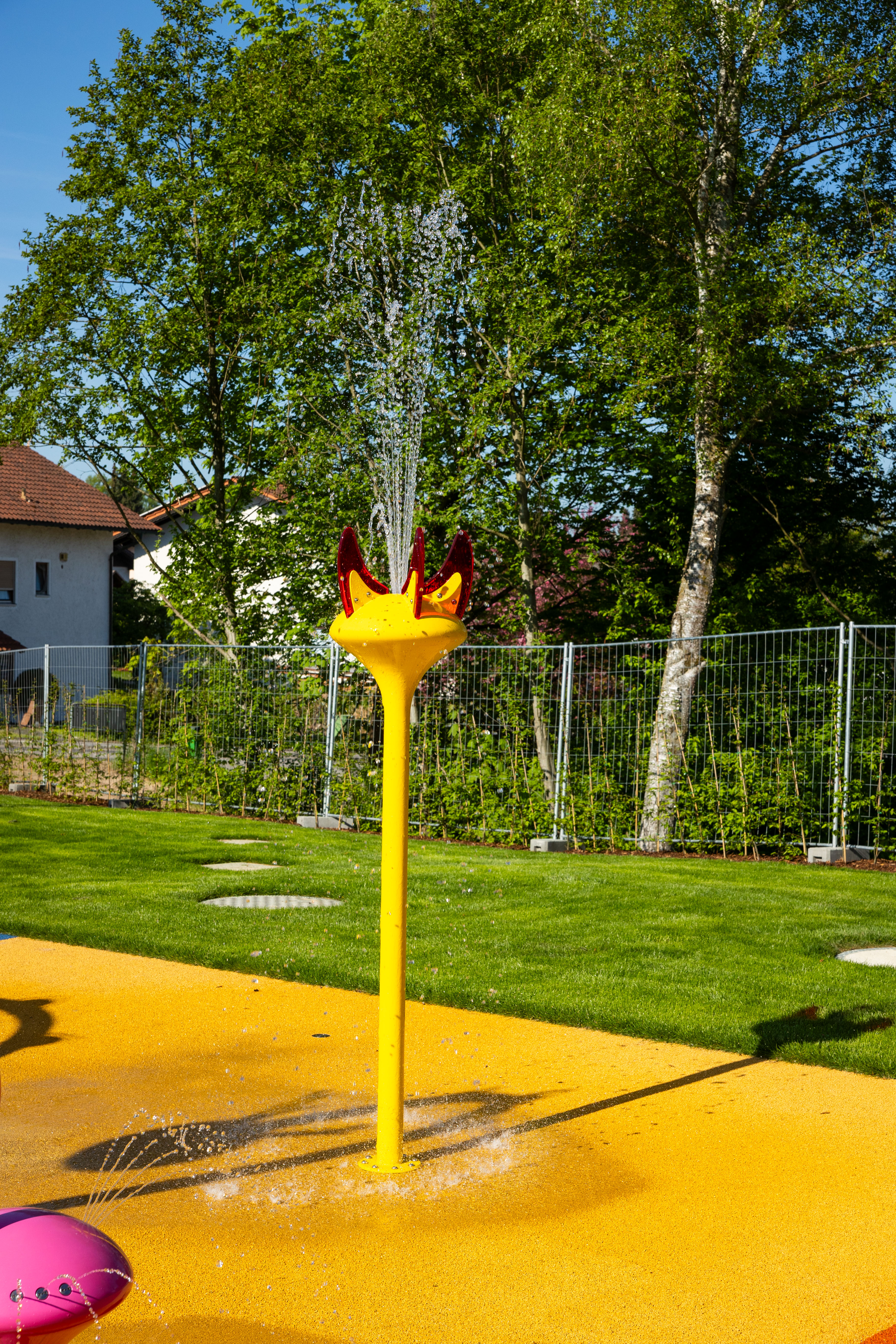 Spritzender Wasserstrahl aus gelber Spielstation im Freibad
