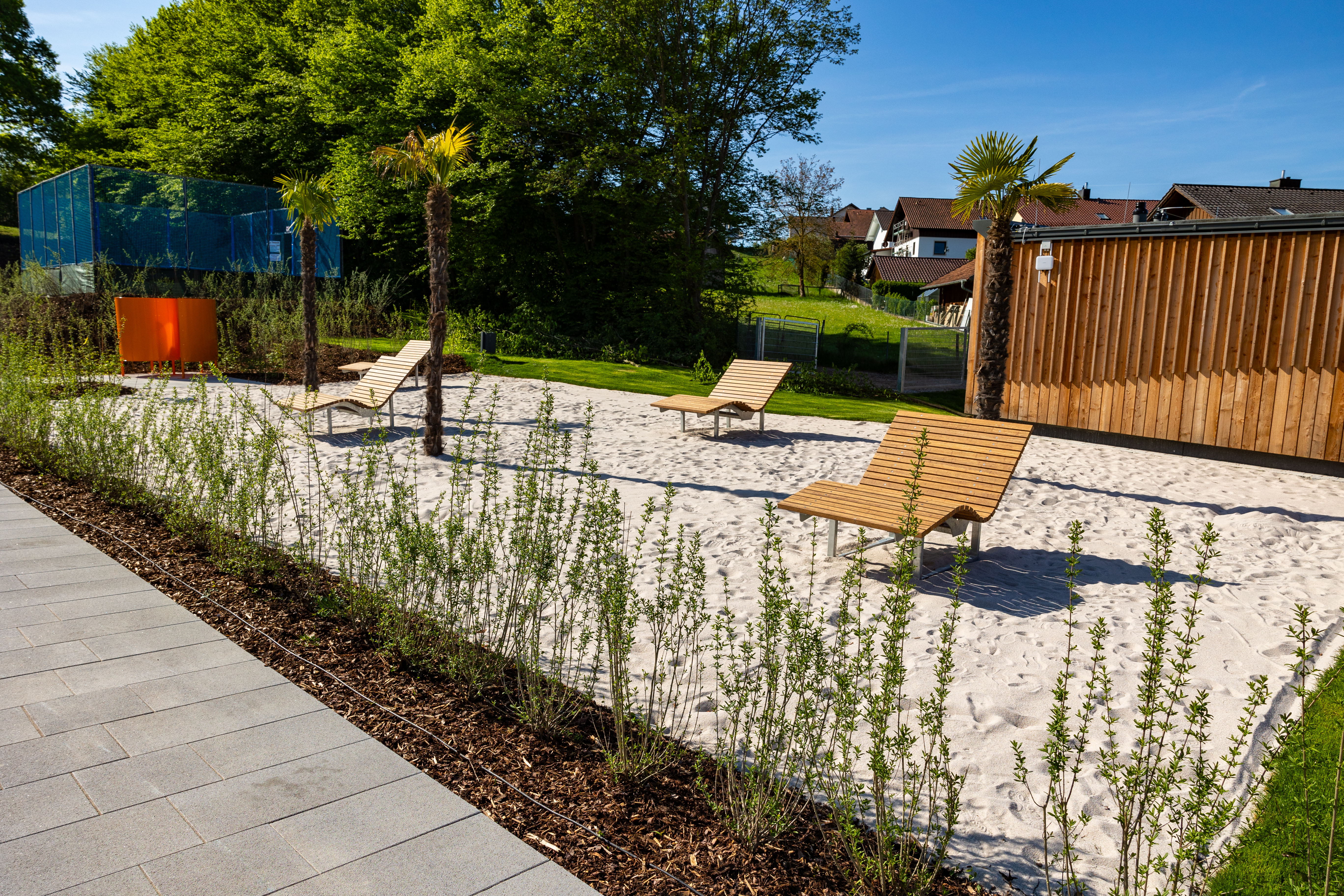 Sonnenschirme und Liegen auf Sandfläche im Freibad