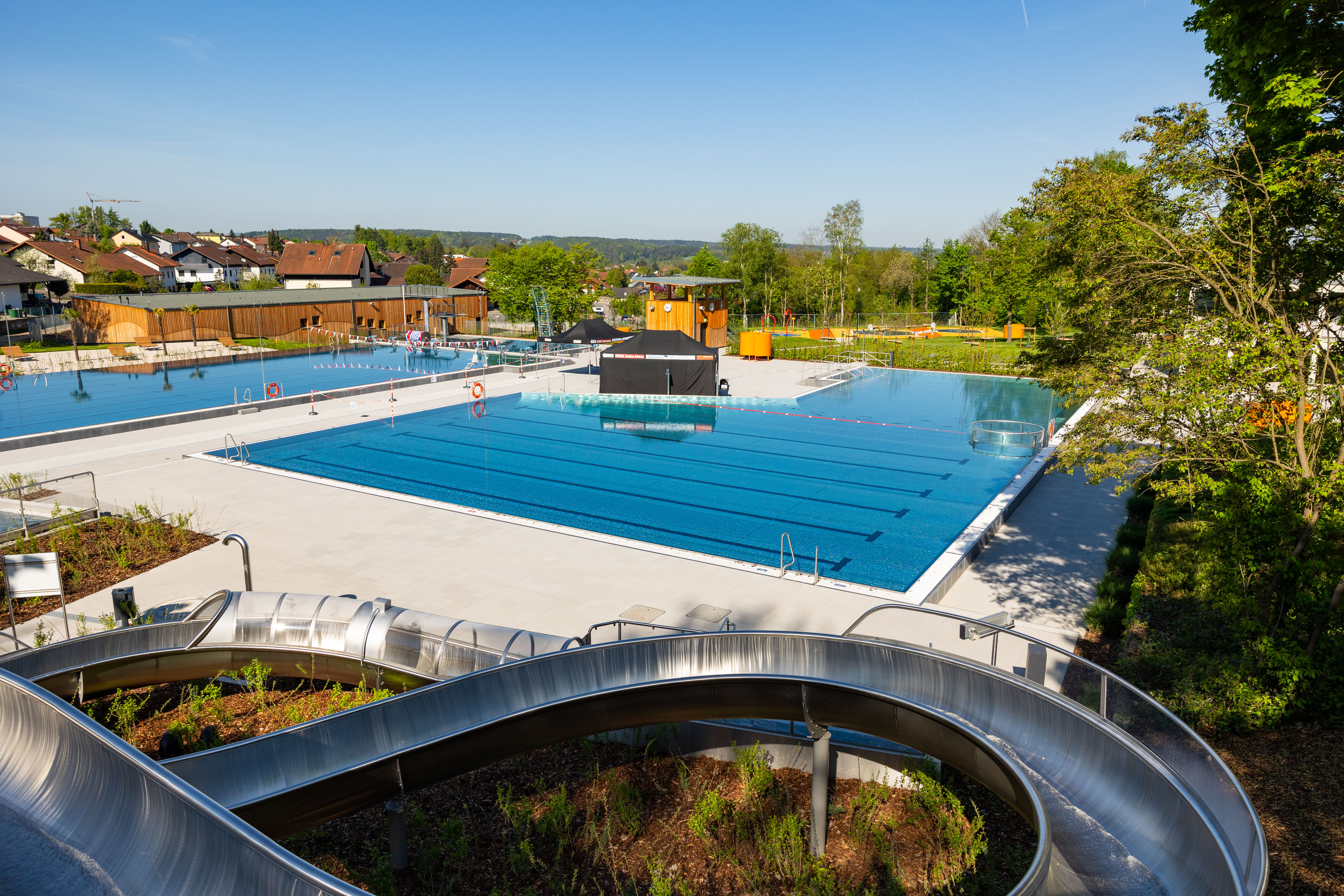Weitblick auf das Freibad mit blauen Wasserbecken und Rutsche.