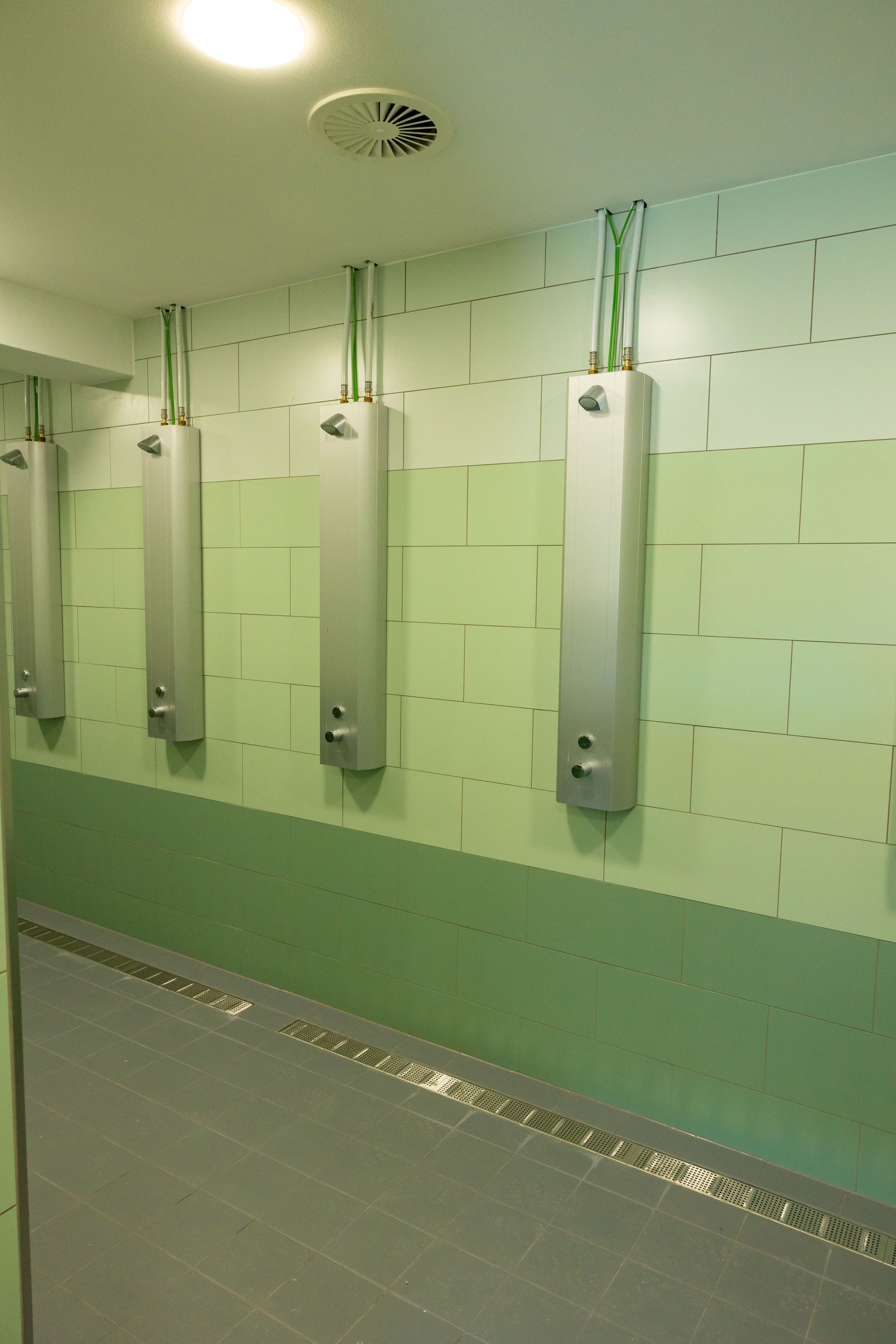 Fünf Duschsäulen an einer grünen Wand im Duschbereich