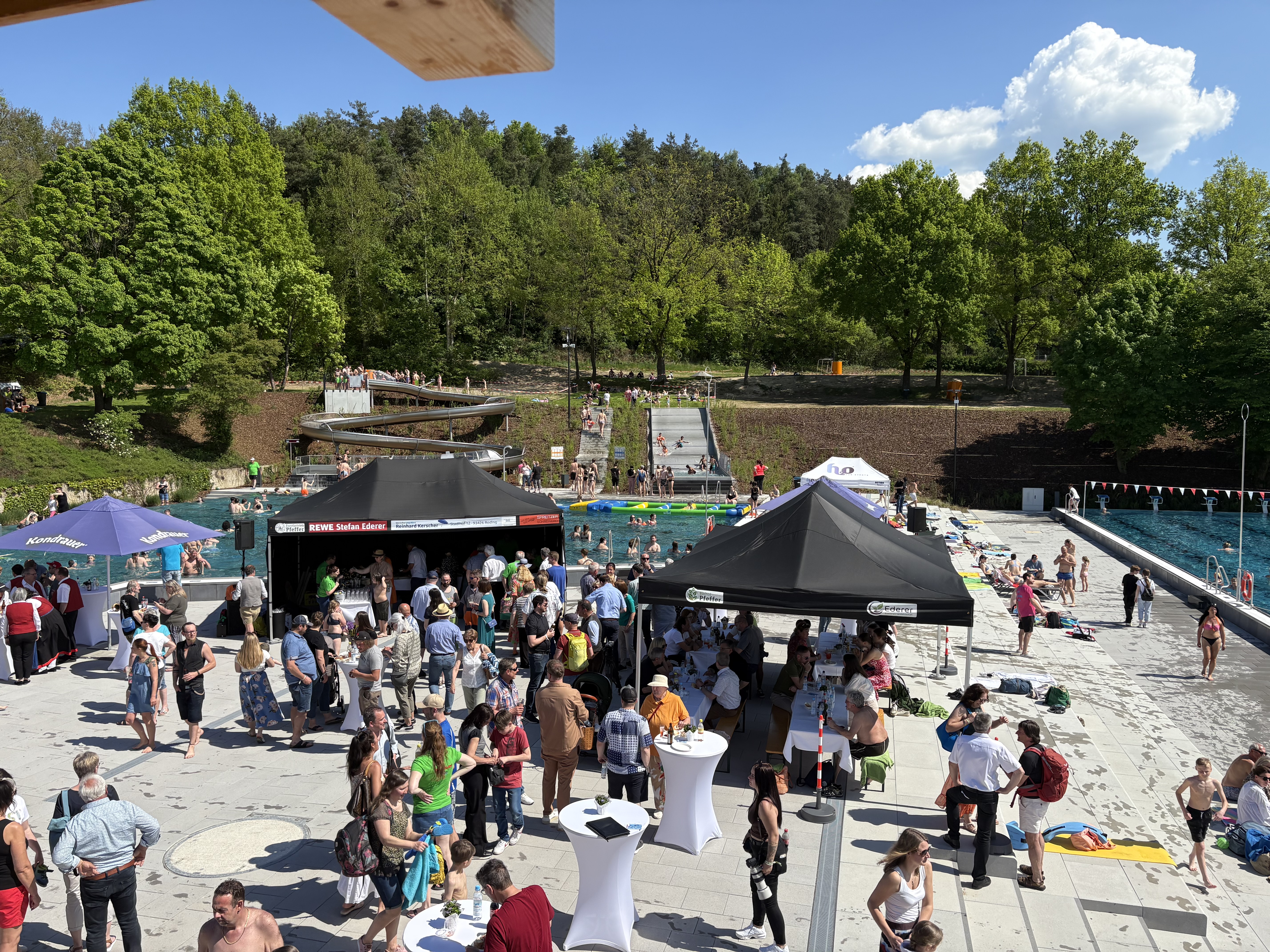Menschenmenge am Freibad mit Schwimmern und Ständen.