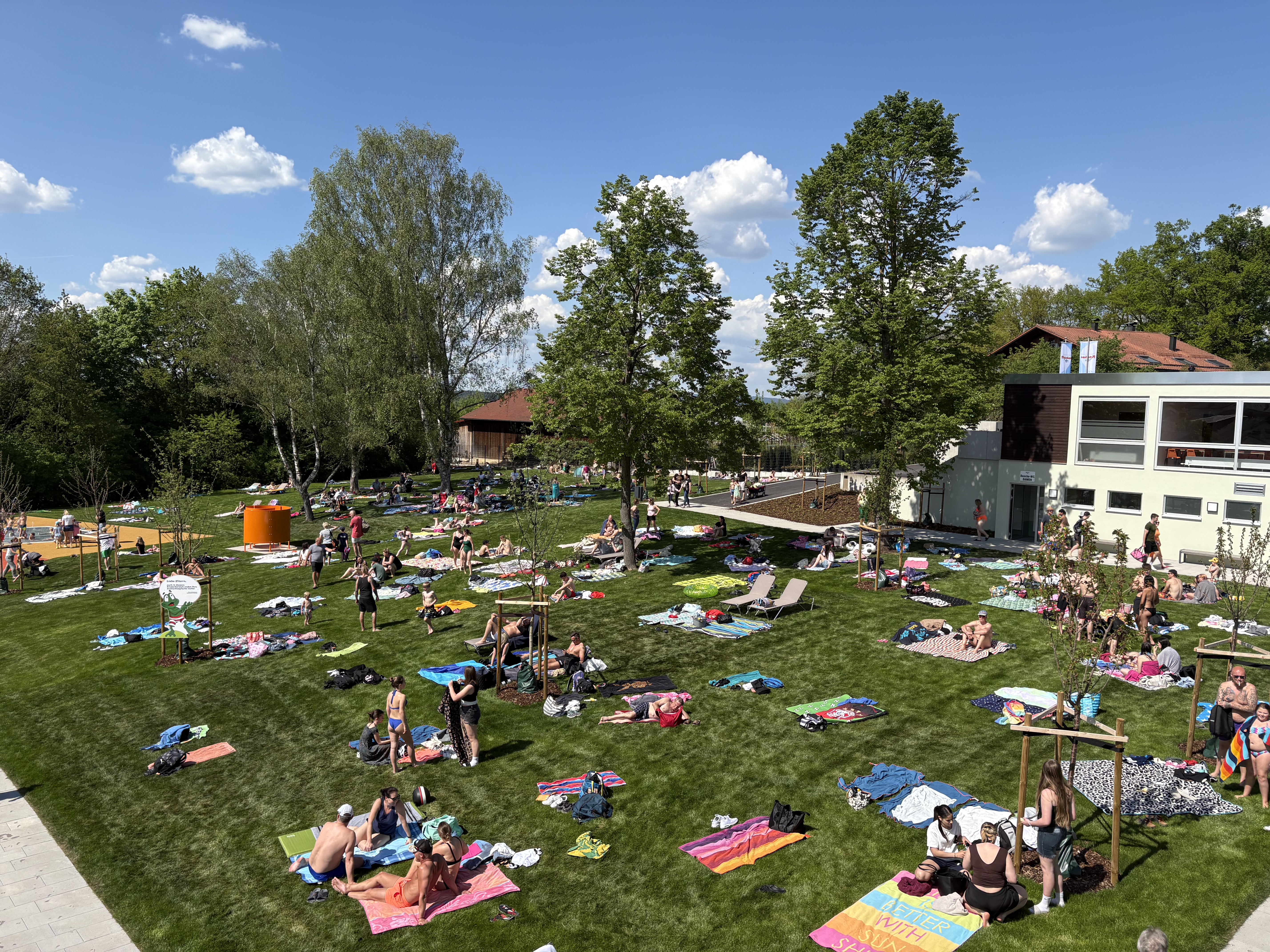 Menschen entspannen auf Wiesen im Freibad bei Sonnenschein.